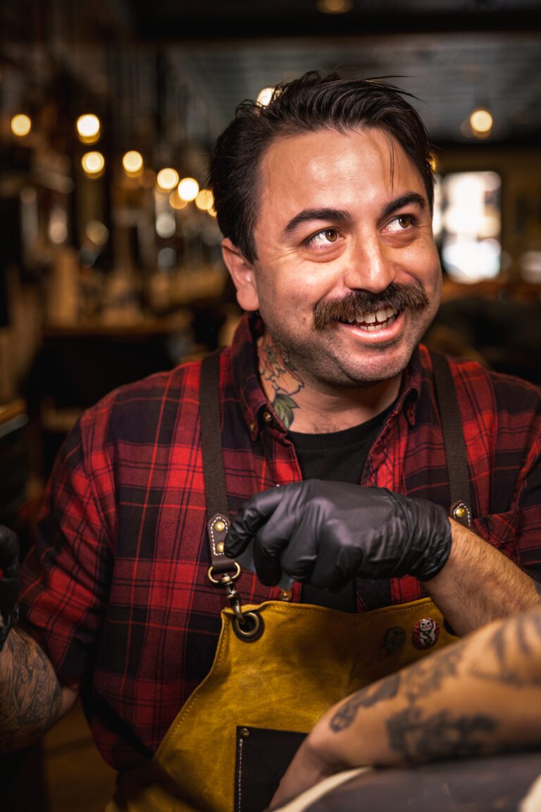 Action portrait of Jandro Sanchez smiling while tattooing