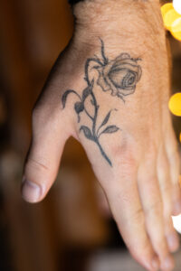 A healed, single-needle wilted rose tattoo on a hand.
