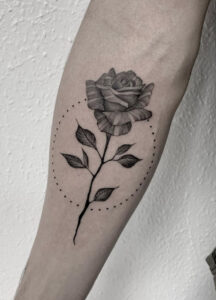 Image of a fineline blackwork styled rose tattoo with a dotted circular frame
