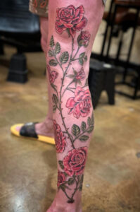 A tattoo of a rose vine climbing from ankle to above knee 